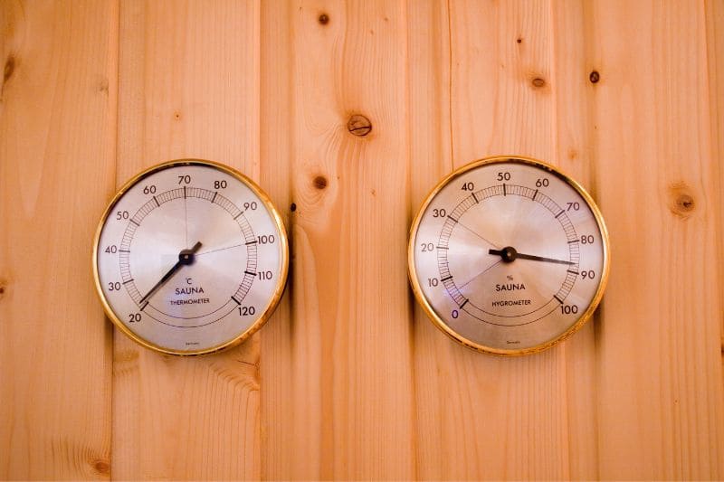 Sauna thermometer and hygrometer mounted on wooden wall, displaying temperature and humidity