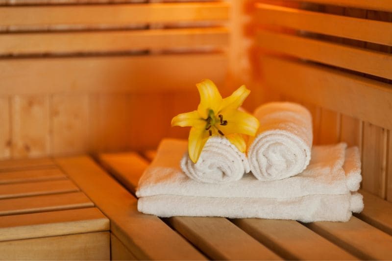 Wooden sauna bench with white towels and yellow lily flower, creating a relaxing spa atmosphere