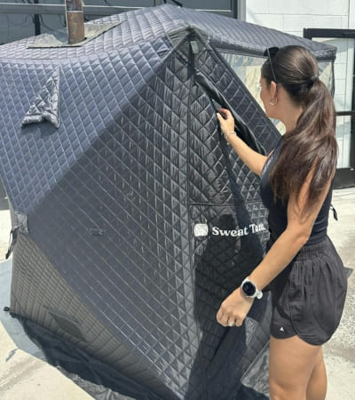 Woman setting up the Sweat Tent Portable Outdoor Sauna, showing ease of assembly