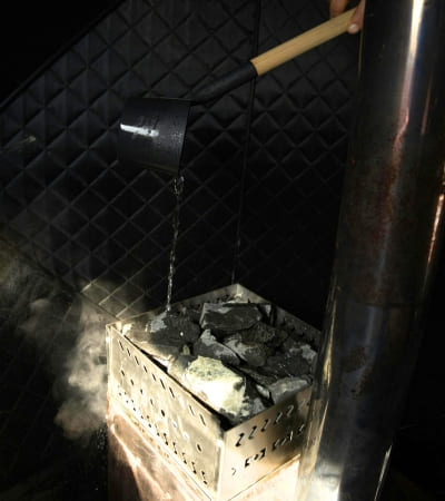 Water being poured over hot rocks in Sweat Tent Sauna, creating steam