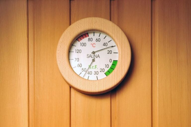 Round thermometer showing sauna temperature and humidity in a traditional Finnish sauna