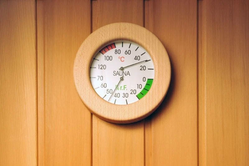 Round thermometer showing sauna temperature and humidity in a traditional Finnish sauna