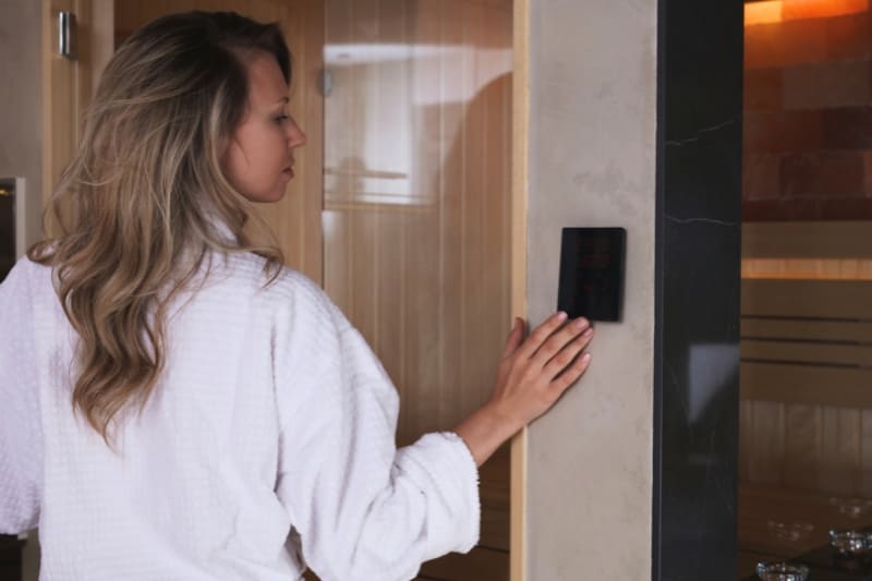 Woman in white robe adjusting digital control panel of an infrared sauna