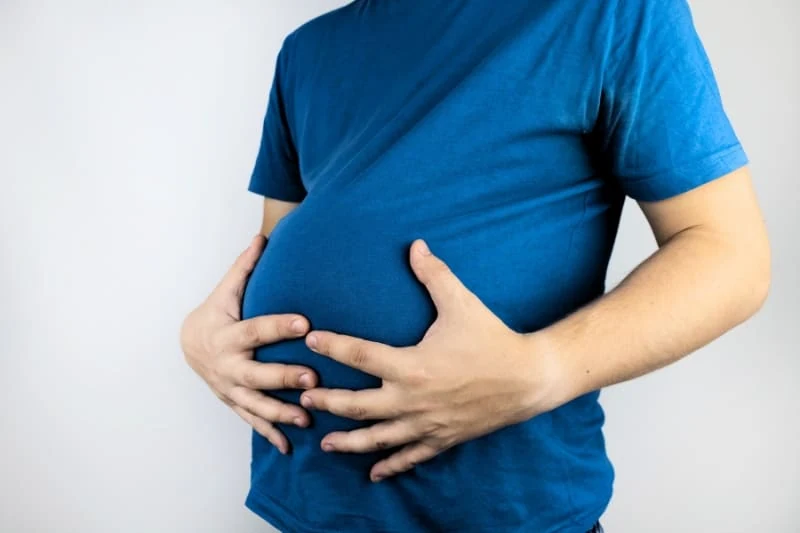 Man holding his bloated stomach, showing discomfort from abdominal swelling