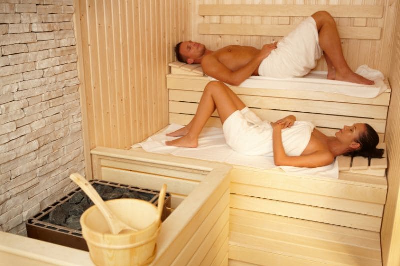 Couple relaxing on tiered benches during sauna session for wellness