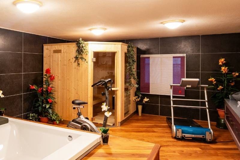 Gym with wooden sauna cabin, exercise equipment, and bathtub