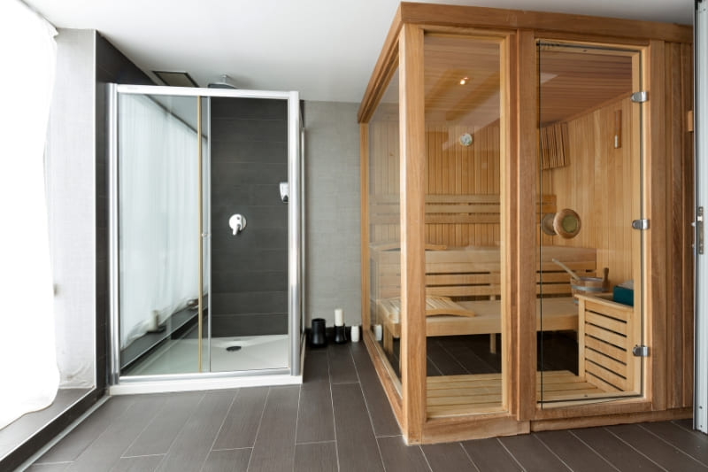 Gym setup with wooden sauna cabin and glass shower enclosure