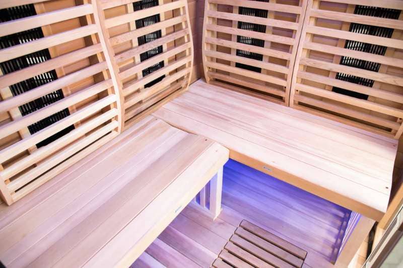 Interior of an infrared sauna showing wooden benches and built-in heaters with blue ambient light