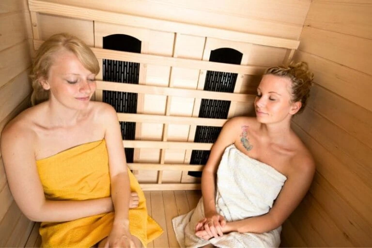 Two women relaxing in an infrared sauna, highlighting the potential health benefits and concerns about cancer risk from infrared heat exposure.