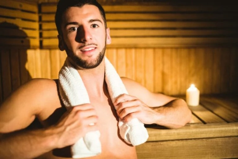 Young man with white towel relaxing in traditional wooden sauna with warm lighting