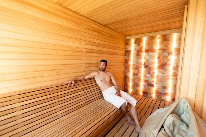 Man relaxing in infrared sauna with illuminated salt wall feature