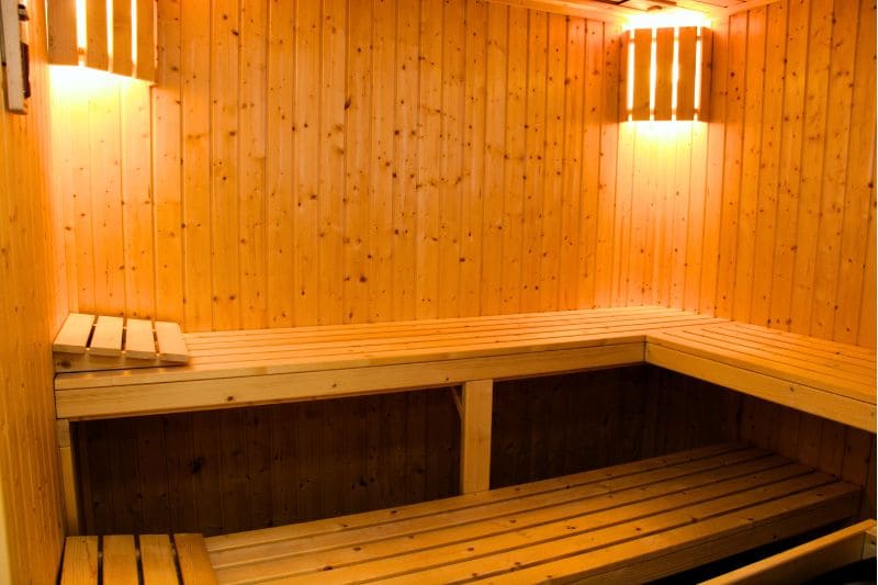 Minimalist sauna design with L-shaped wooden benches, pine wall panels and modern sconce lighting