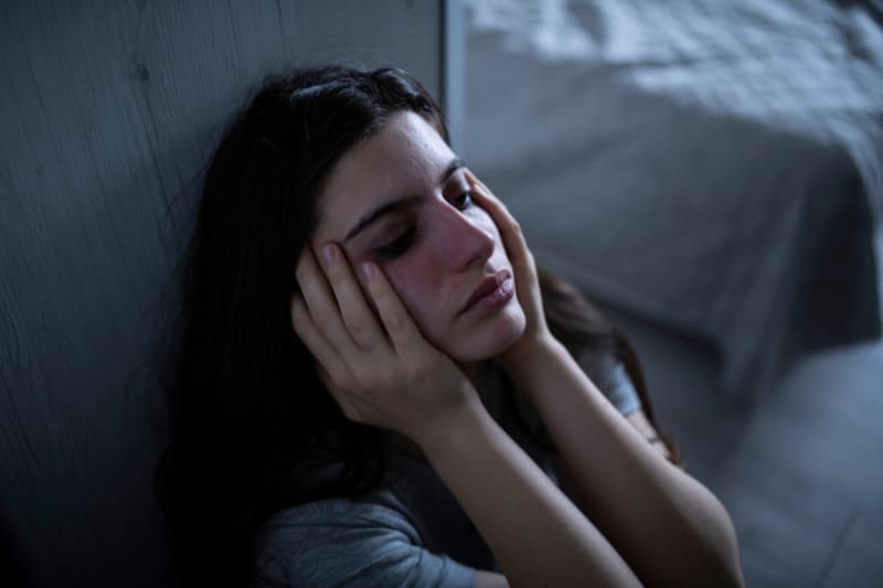 Woman sitting in a dimly lit room, showing signs of distress and anxiety, highlighting emotional struggle.