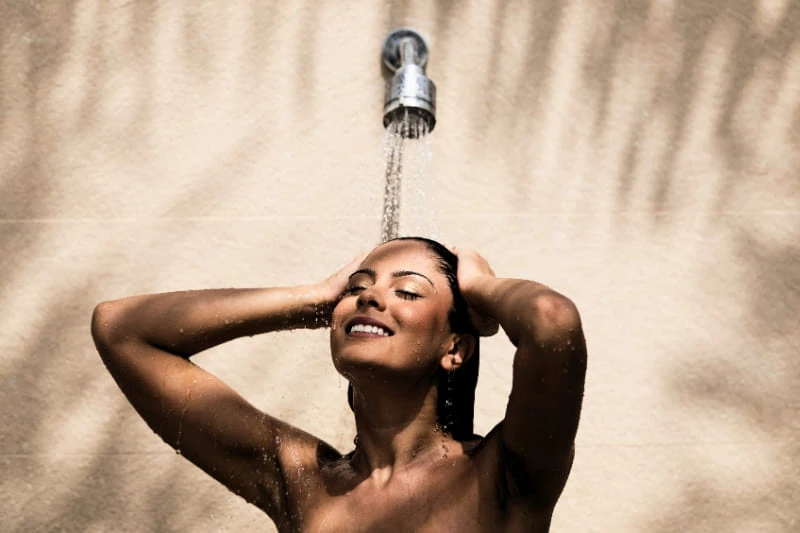 A woman enjoying a refreshing shower after sauna, rinsing off under flowing water.