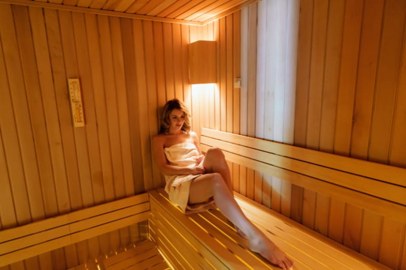 Woman relaxing in a wooden sauna, wrapped in a towel, enjoying the calming benefits of sauna for anxiety relief.