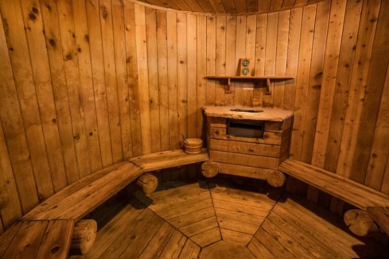 Rustic sauna interior featuring natural log benches, knotty pine walls and traditional wooden accessories