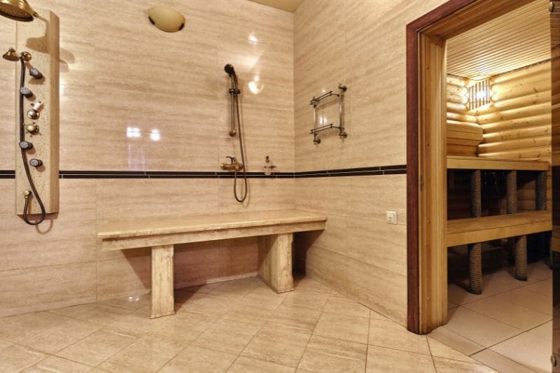 Shower station in a sauna room with tiled walls and wooden benches.