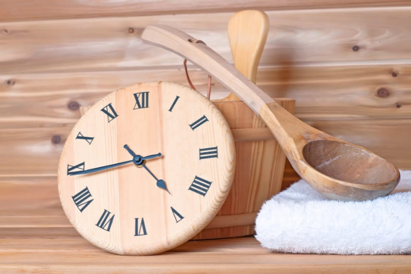 Sauna accessories inside a sauna including a wooden clock for timing sauna therapy sessions