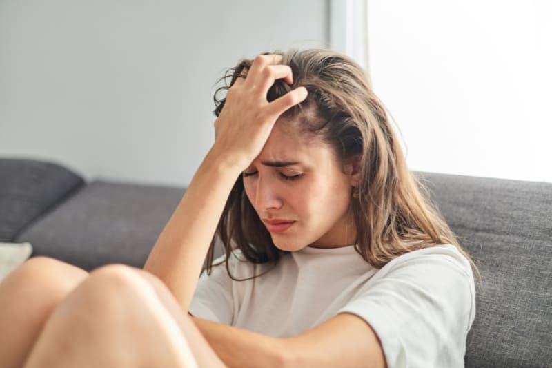 Woman looking stressed and holding her head, showing the symptoms of anxiety and tension.