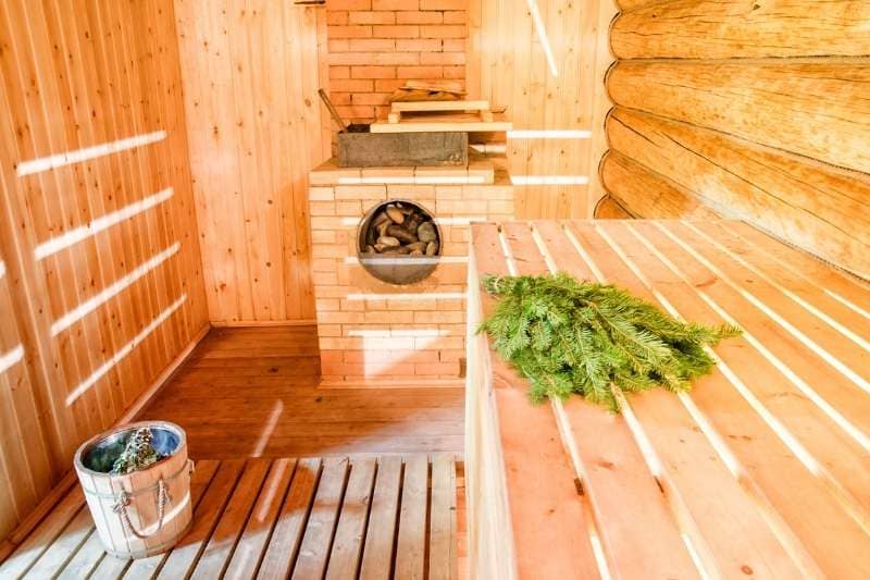 Finnish sauna with brick heater design, wooden benches and traditional sauna accessories including eucalyptus sauna whisk