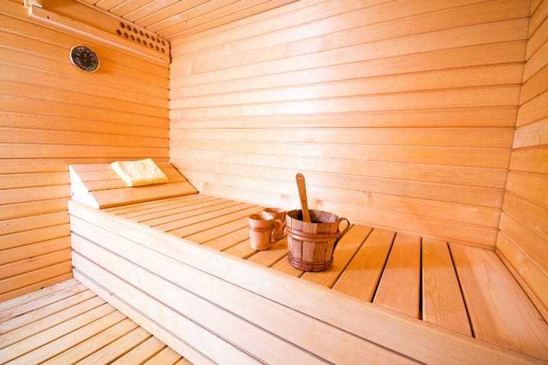 Traditional Finnish sauna interior with light wood paneling, ergonomic bench design and traditional water bucket