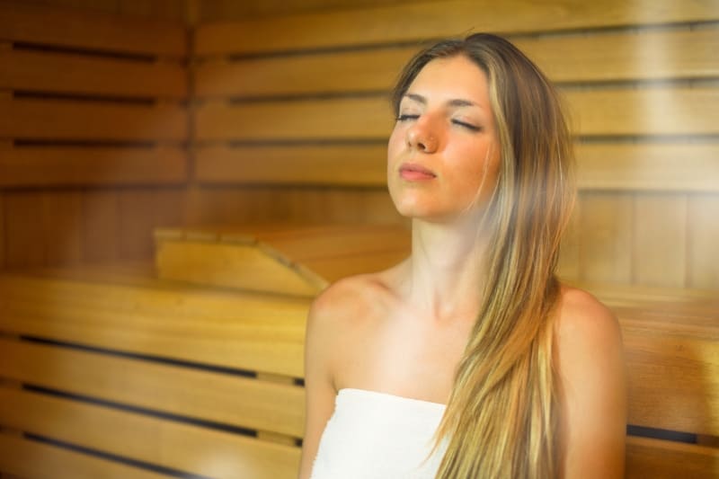 Woman with long blonde hair relaxing in a wooden steam room with eyes closed