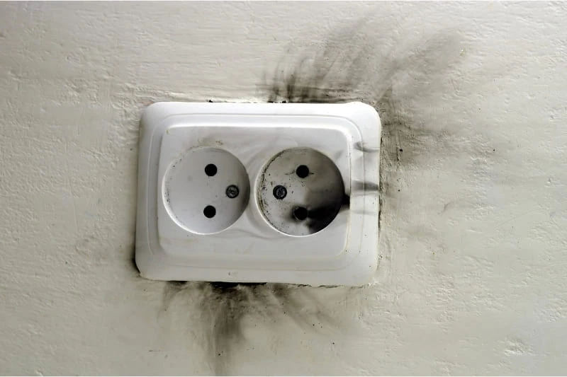 Dangerous electrical hazard shown by dark scorch marks surrounding a standard wall outlet, demonstrating why every sauna cannot be plugged into a regular outlet.