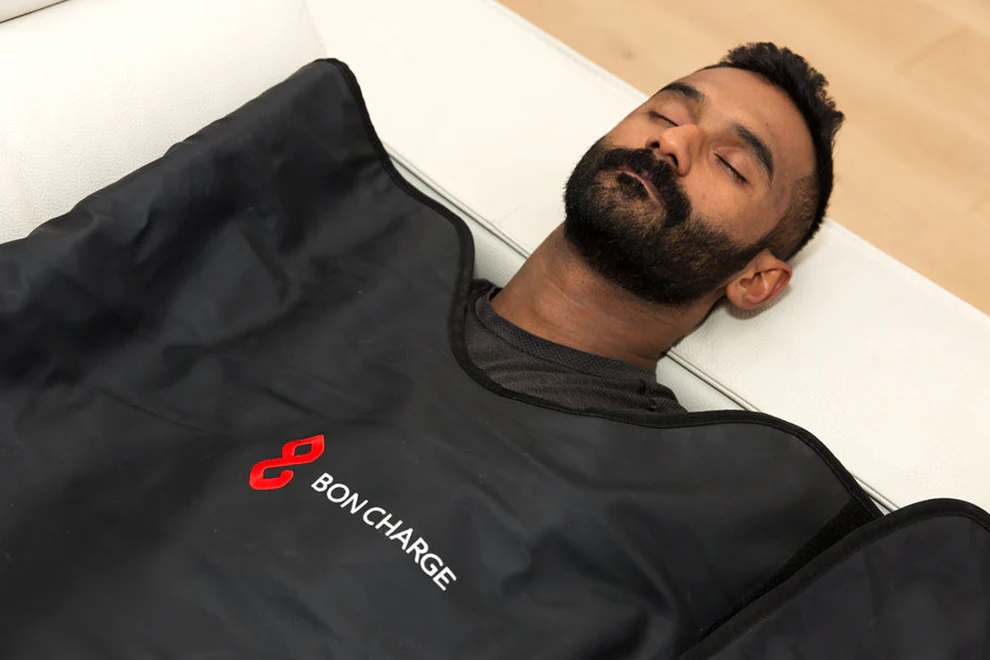 Person lying down relaxing during an infrared sauna session in BON CHARGE sauna blanket on white couch