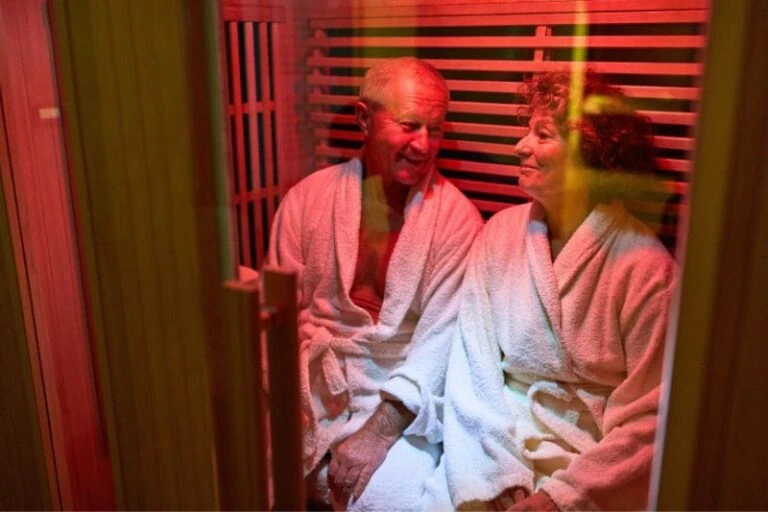 Senior couple relaxing in white robes during infrared sauna therapy session with therapeutic red light