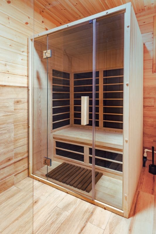 Full view of contemporary infrared sauna interior with glass door, wooden benches and heating panels