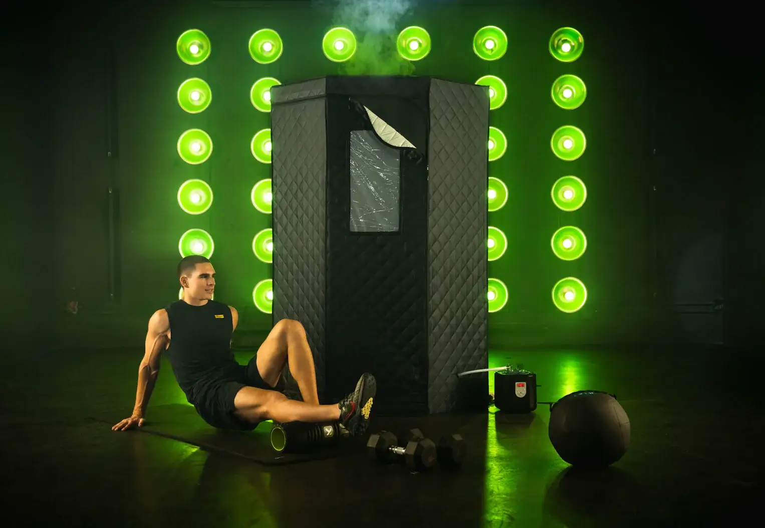 Athletic performance recovery setup with Saunabox portable sauna, exercise equipment, and green lighting backdrop