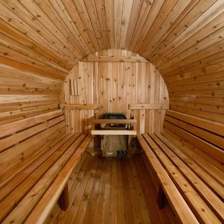 Interior view of wooden barrel sauna showing cedar benches, tongue and groove paneling, and centrally mounted sauna heater with ventilation