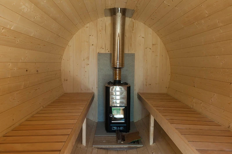 Barrel sauna interior showing wood-burning stove installation and cedar bench seating, demonstrating proper sauna ventilation setup