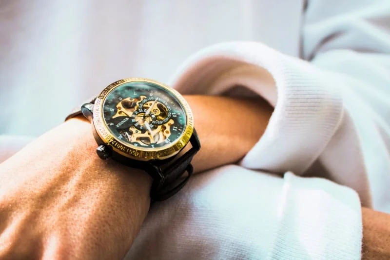 Gold-tone mechanical watch with visible movement mechanism worn on wrist with white sleeve