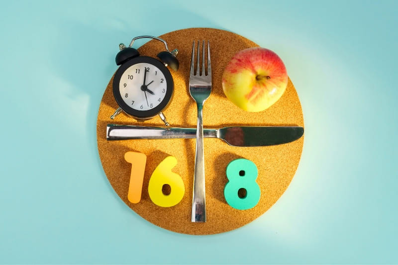 Creative composition showing 16:8 intermittent fasting method with clock, cutlery, apple and numbers on golden circular board against turquoise background