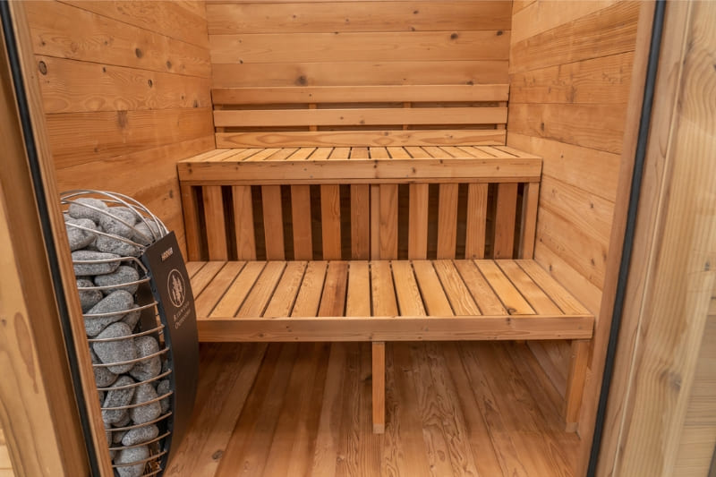 Interior view of Redwood Outdoors Cabin 4-person sauna showing two-tier bench seating and an electric sauna heater with stones inside