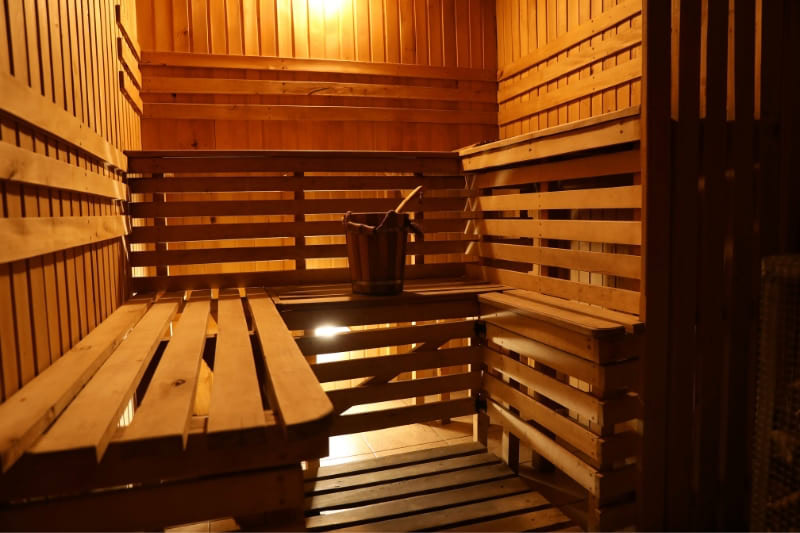 Empty traditional wooden sauna interior with tiered benches and water bucket, warm ambient lighting