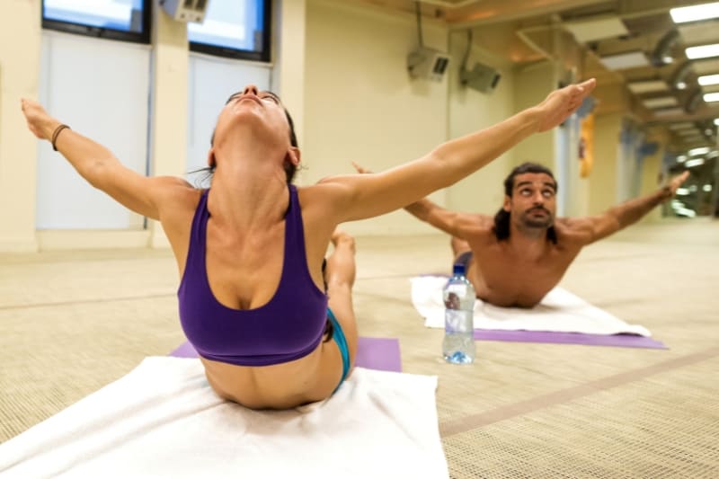 Hot yoga practitioners performing Poorna Shalabhasana (full locust pose) during intense heated yoga session