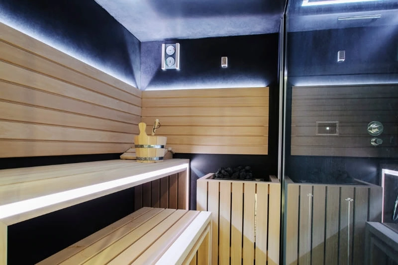 Contemporary private sauna room interior with tiered wooden benches, LED lighting, and glass door, modern spa design