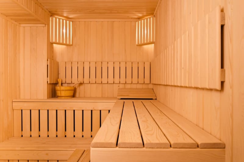 Clean minimalist Finnish sauna interior with light wood paneling, tiered benches, and water bucket in corner