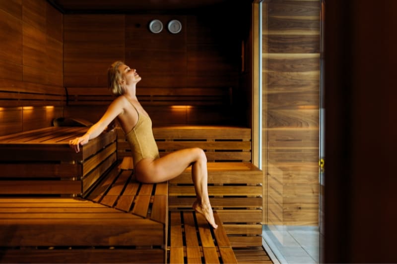 Modern luxury sauna interior with a lady in swimsuit reclining on wooden benches, spa relaxation atmosphere