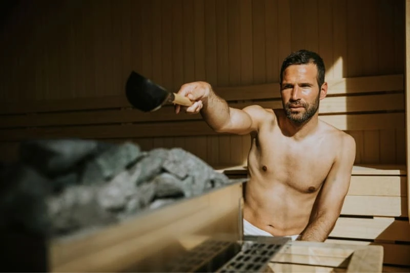 Man pouring water on sauna stones in modern wooden sauna for an authentic Finnish sauna experience