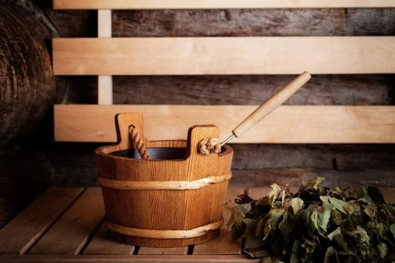 Traditional wooden sauna bucket with ladle and fresh birch leaves for aromatherapy on wooden bench