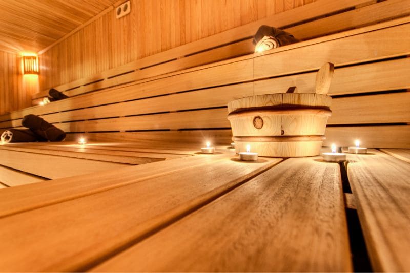 Sauna interior with lit candles and wooden water bucket on wooden benches creating warm ambiance