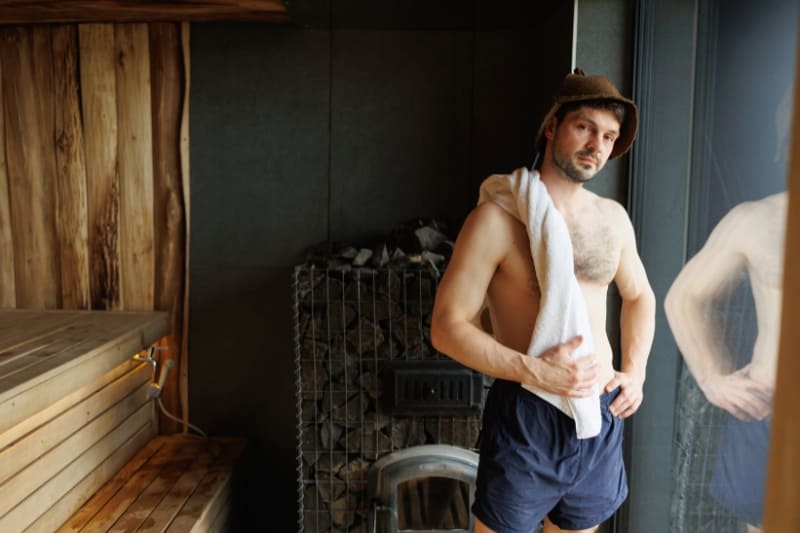 Man with towel cooling down after sauna session in wooden sauna room with stacked firewood