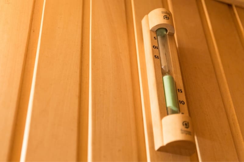 Wooden mounted sand timer for tracking sauna session duration mounted on pine wall panels