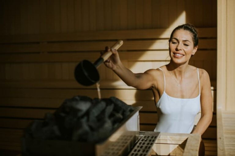 Woman in white adding water to sauna stones, creating therapeutic steam in traditional Finnish sauna