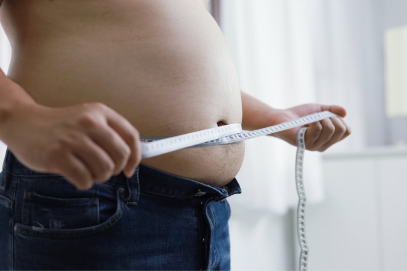 A man measuring his waist with tape measure, illustrating common misconception about sauna weight loss being permanent