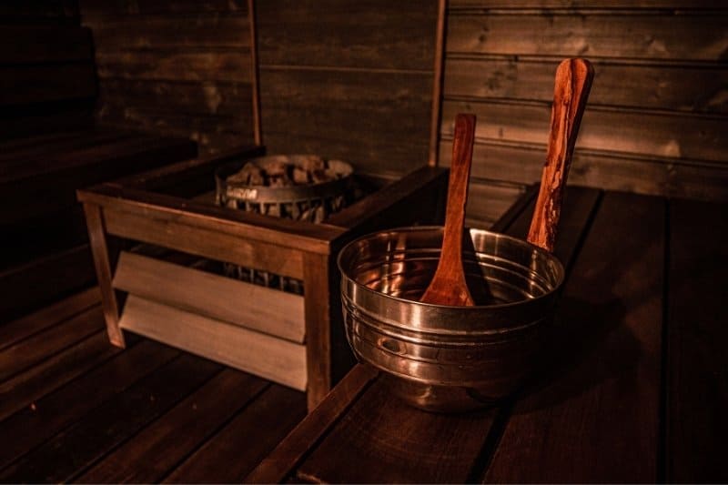 Traditional wooden sauna interior with water bowl and ladles in dim lighting creating relaxing atmosphere