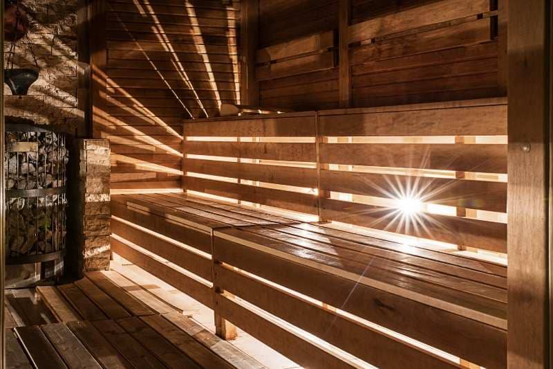 Interior of wooden sauna with sunlight beaming through slats creating dramatic ray patterns across wooden benches